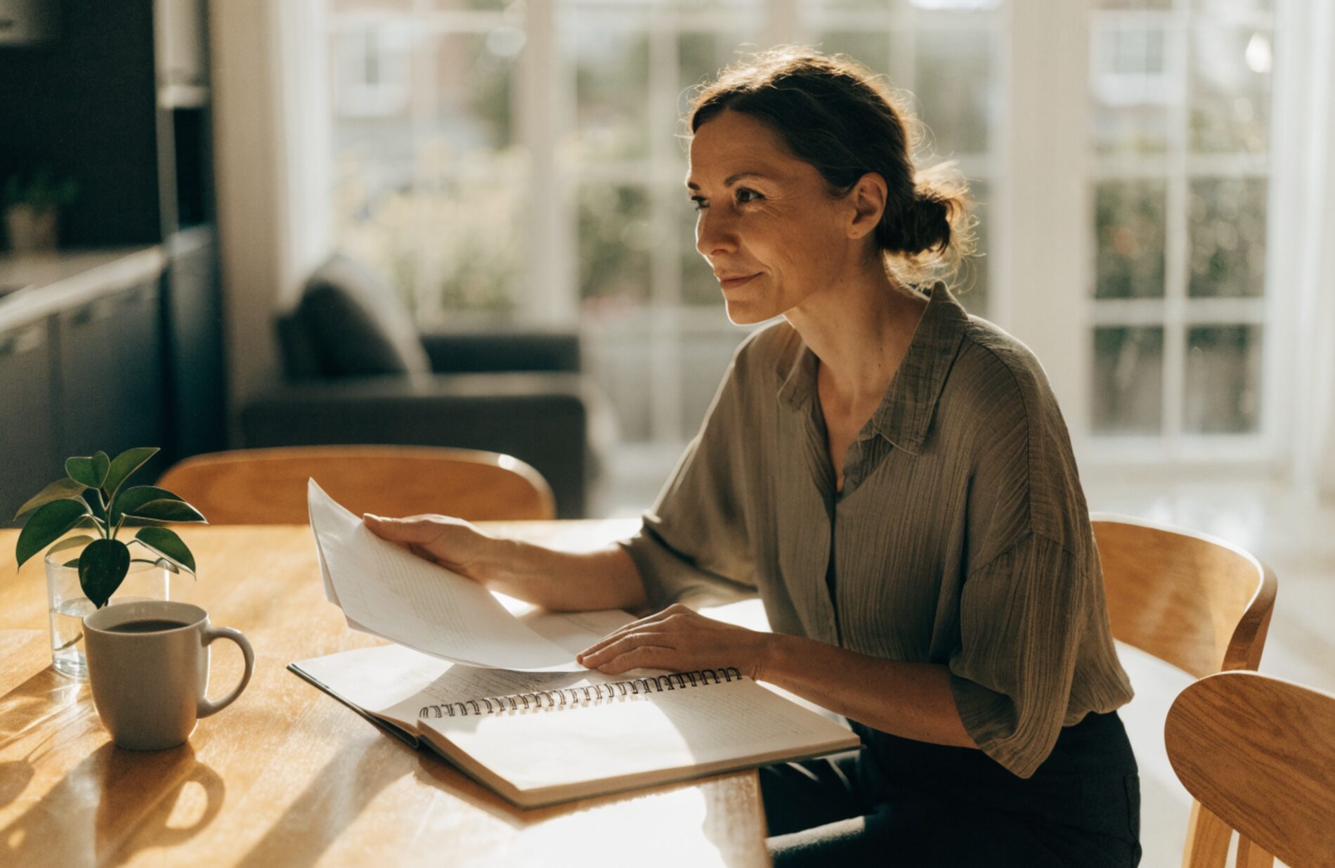 A person calmly organizing divorce paperwork at a sunlit table, looking forward with quiet resolve